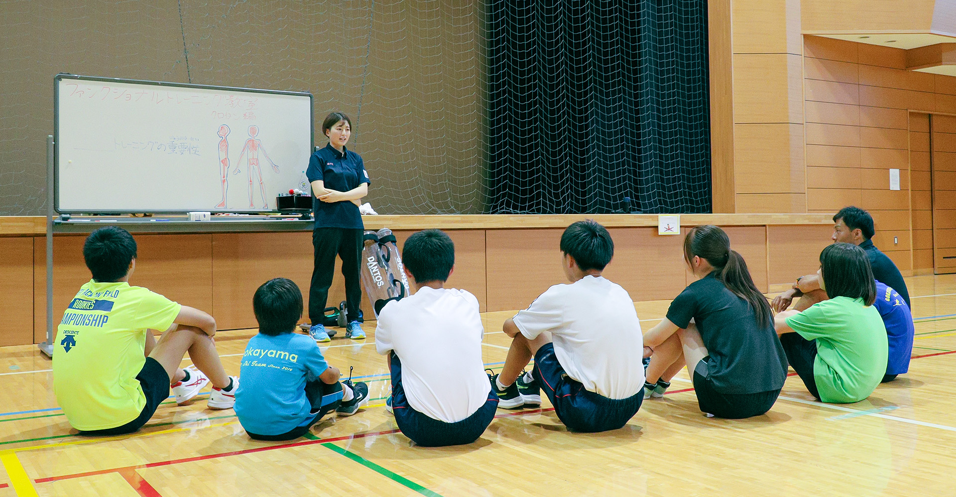 体育館で代表の前に座っている子どもたち